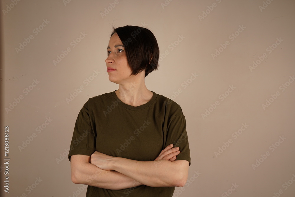 Obraz premium A brunette girl with short hair and gray eyes. She crossed her arms in front of her and looks in the other direction. The girl is found. On a beige background.