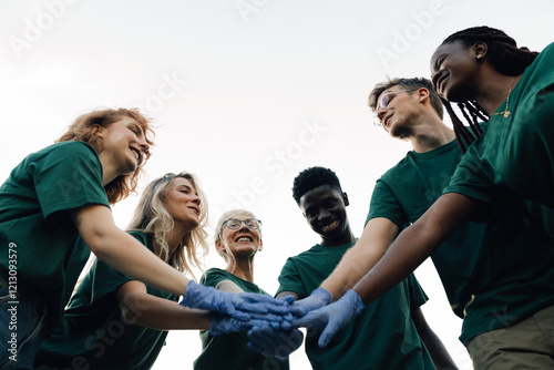 Happy volunteers joining hands wearing gloves before volunteering