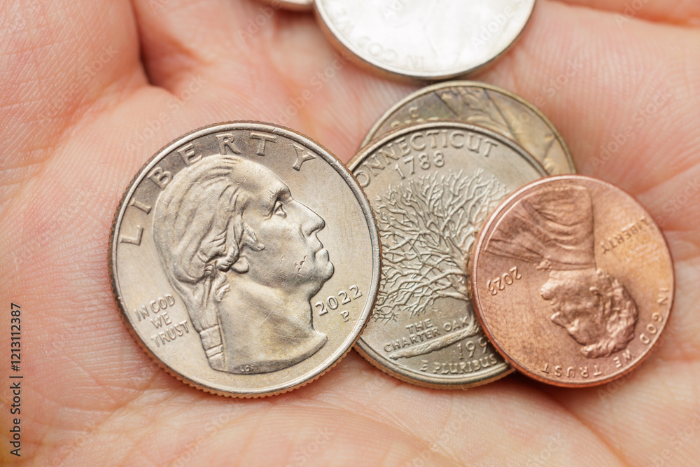 A hand is holding a collection of coins, including a silver Liberty coin A hand is holding a collection of coins, including a silver Liberty coin