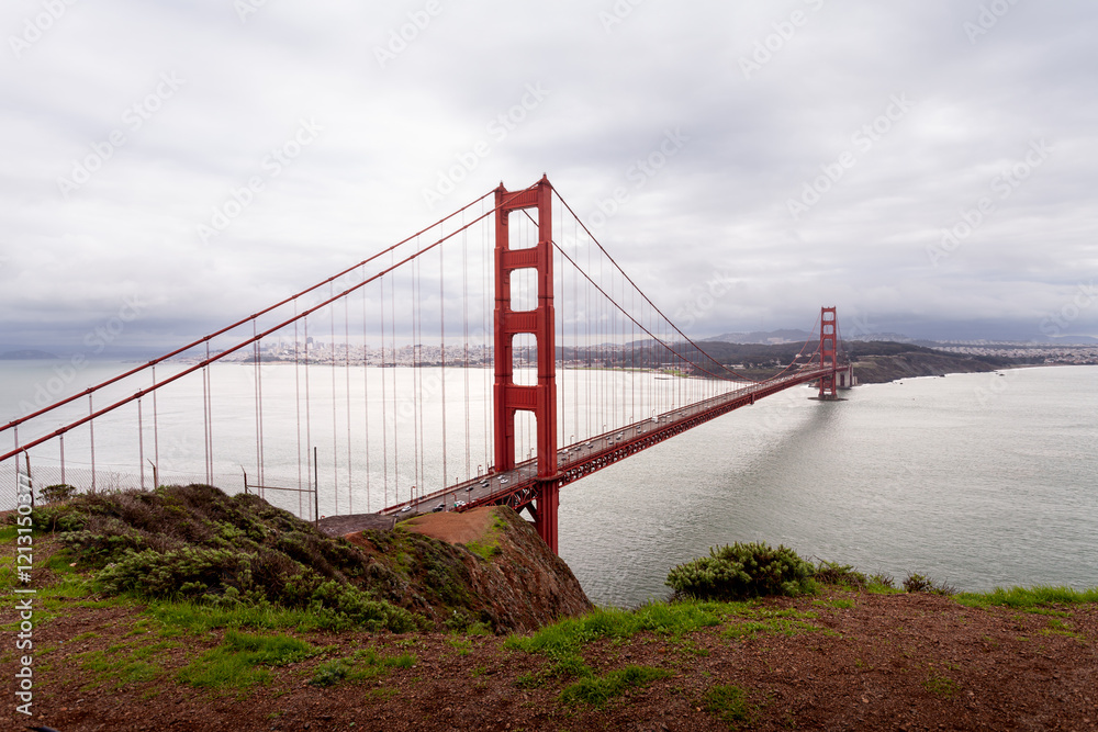 Fototapeta premium Iconic Golden Gate Bridge spans tranquil waters under moody clouds in San Francisco.