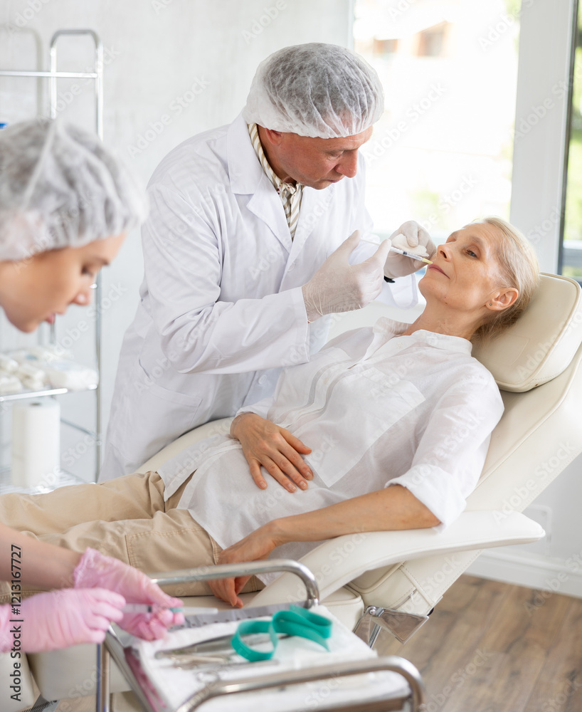 Obraz premium Adult woman applying rejuvenating treatments by mature doctor in cosmetology office. Nurse preparing syringe.