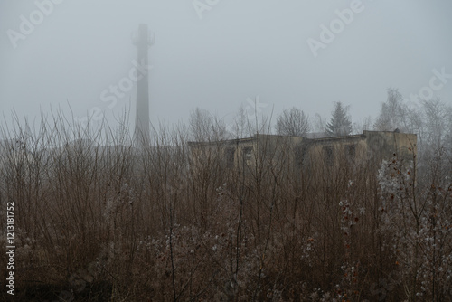 Abandoned and weed-covered industrial area with a building and a tall chimney in winter photo