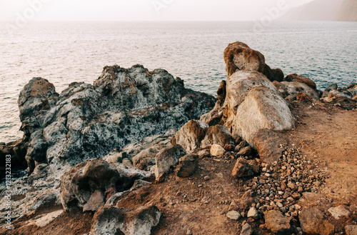 A rugged coastal landscape with weathered rocks and a calm ocean at sunset