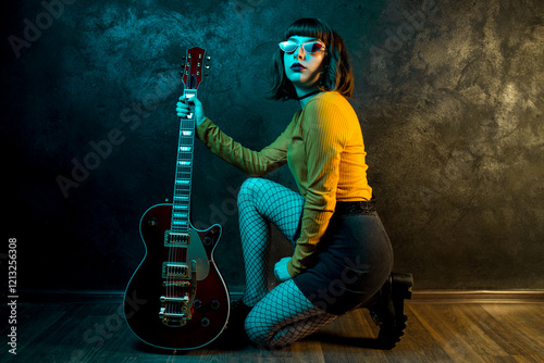 Stylish young hipster woman with curly hair with red guitar in neon lights. Rock musician posing with electrical guitar.