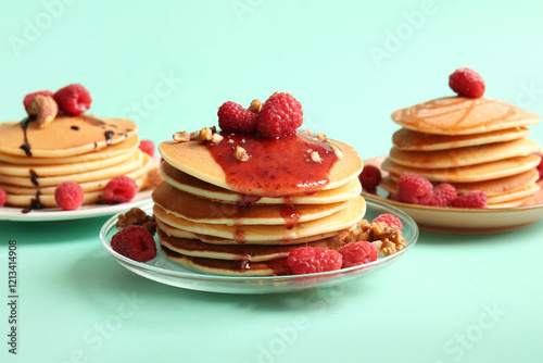 Plates of tasty pancakes with raspberries and nuts on turquoise background photo