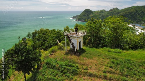 View A man stands on a viewing tower in the coastline with hills, coral cliffs, waves from the ocean in Watu Bale Beach Kebumen  Indonesia photo