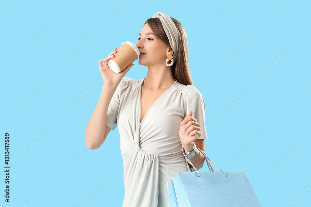 Beautiful stylish young woman with shopping bags drinking coffee on blue background