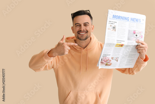 Happy young man pointing at newspaper on beige background