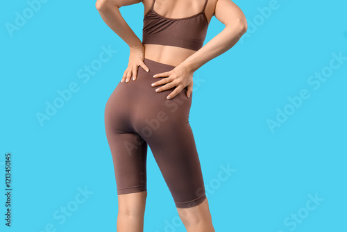 Young woman in cycling shorts on blue background, back view