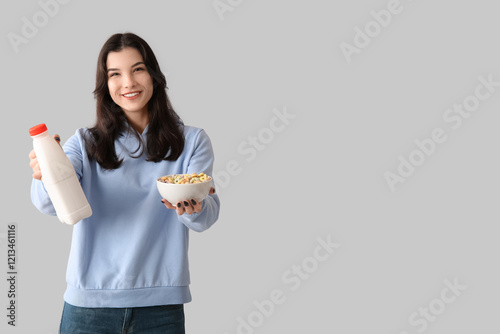 Young woman with bowl of tasty cereal rings and milk on light background