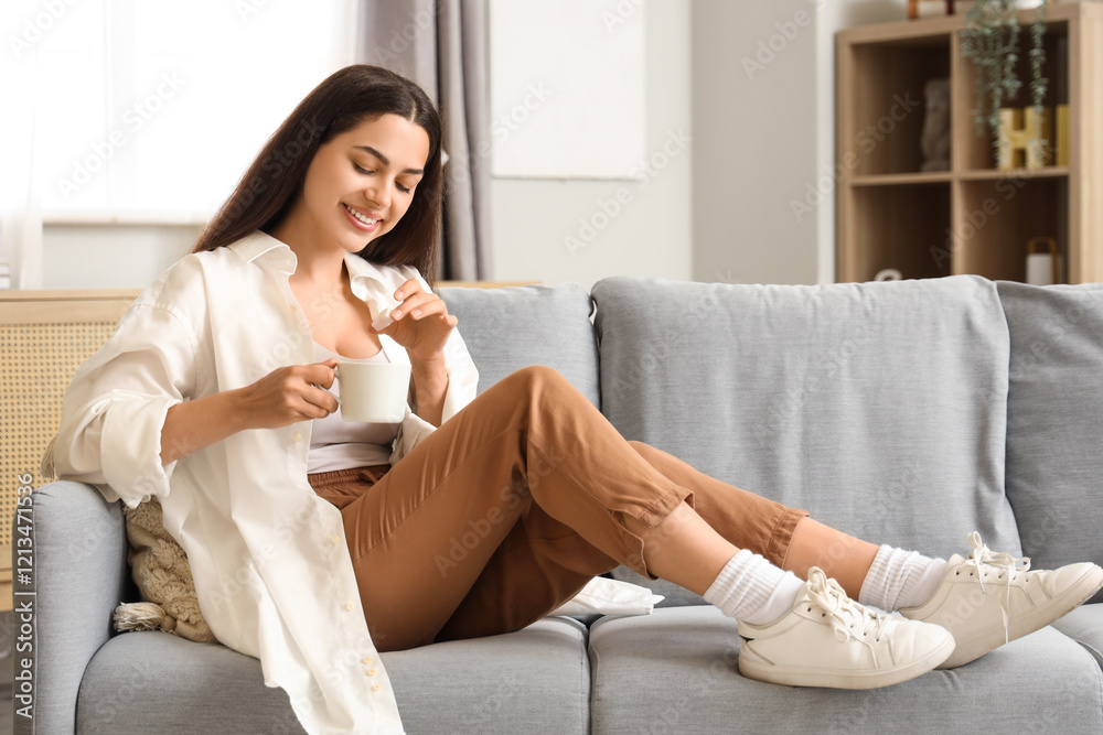 Pretty young woman with cup of hot coffee and sugar sitting on sofa at home Pretty young woman with cup of hot coffee and sugar sitting on sofa at home