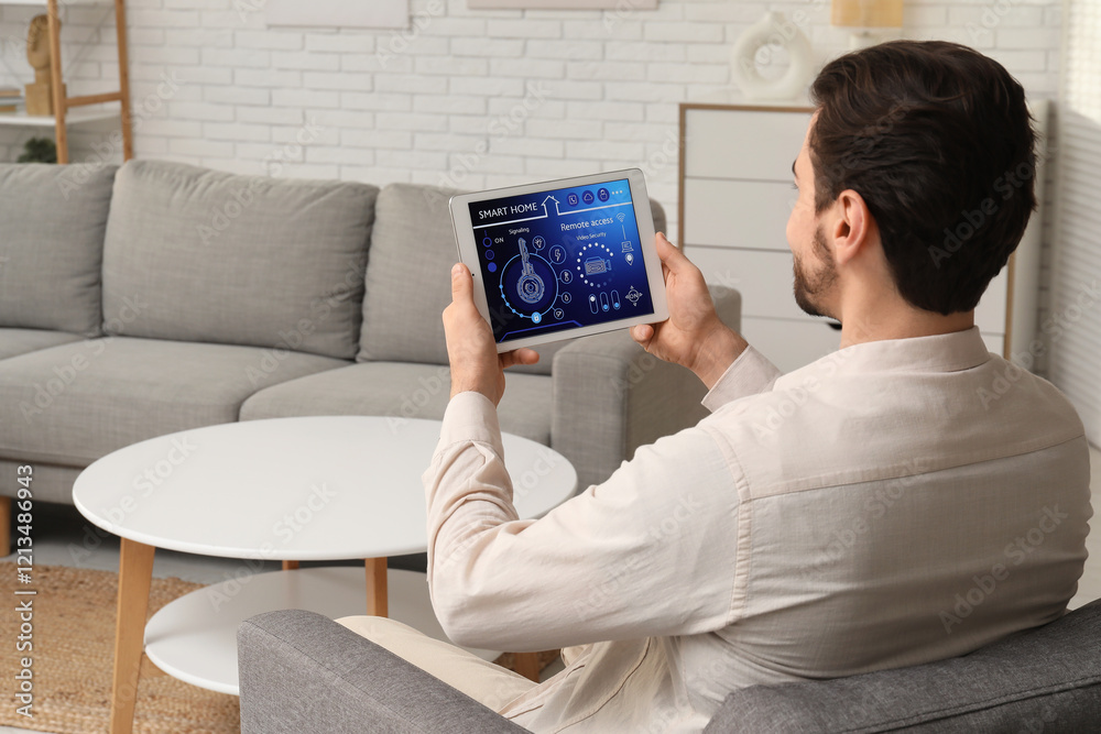 Young man with smart home security system control panel sitting in room, back view Young man with smart home security system control panel sitting in room, back view