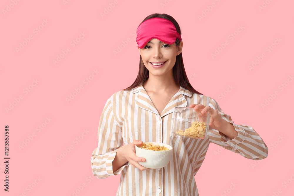 Young woman in pajamas pouring tasty cornflakes into bowl on pink background Young woman in pajamas pouring tasty cornflakes into bowl on pink background