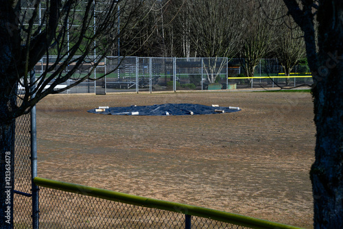 Baseball diamond with the pitcher’s mound covered and protected for winter by a black tarp secured by white weights, sports and recreation background
