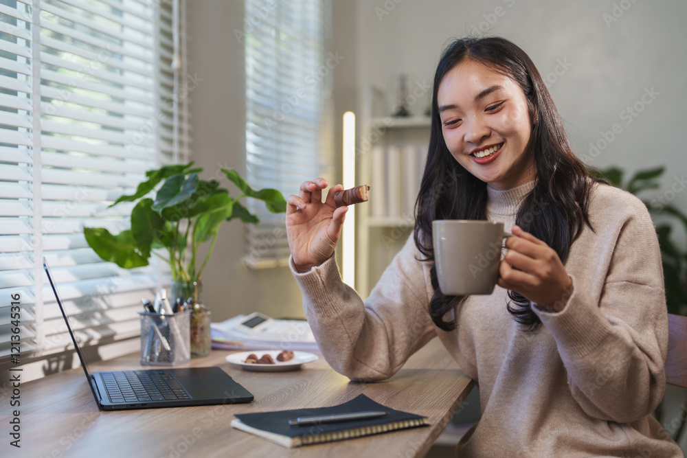 Young asian businesswoman enjoying a relaxing work break at home, savoring a chocolate bar and sipping coffee while sitting at her desk with a laptop and notebook nearby Young asian businesswoman enjoying a relaxing work break at home, savoring a chocolate bar and sipping coffee while sitting at her desk with a laptop and notebook nearby