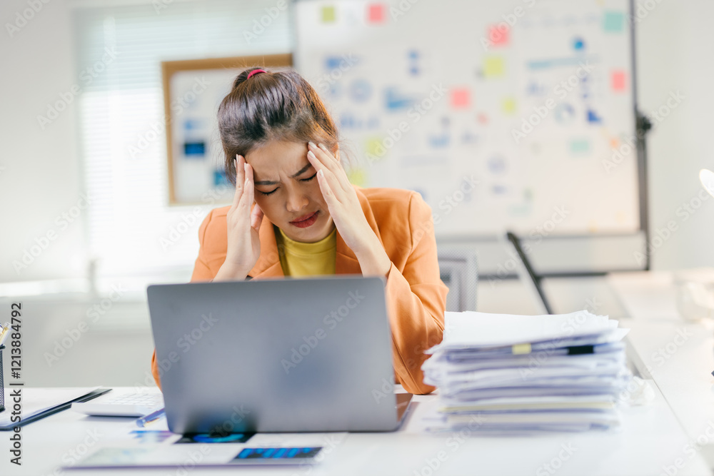 Young asian businesswoman suffering from headache while working on laptop in office with documents on desk Young asian businesswoman suffering from headache while working on laptop in office with documents on desk