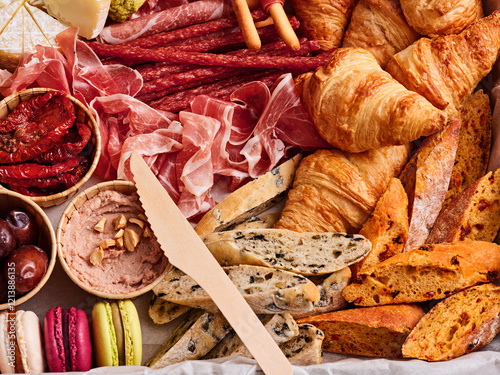 A vibrant display of charcuterie features a variety of cured meats, fresh croissants, gourmet cheeses, and colorful macarons, perfect for a festive gathering or casual dining photo