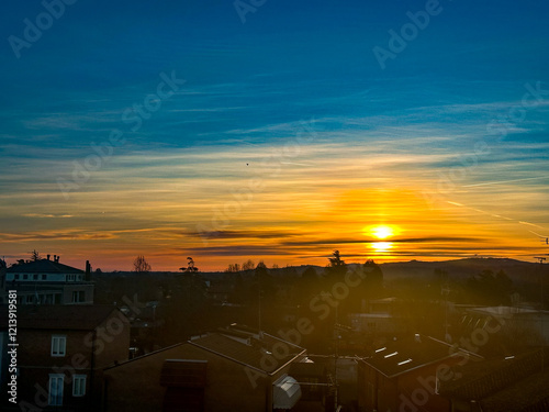 As the sun slowly sets down over the sprawling city, the silhouettes of buildings rise prominently in the foreground against the vibrant sky