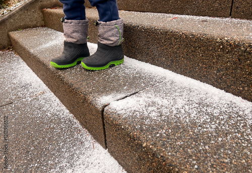 Close up of toddlers feet on stone steps outdoors covered with iced snow and salt