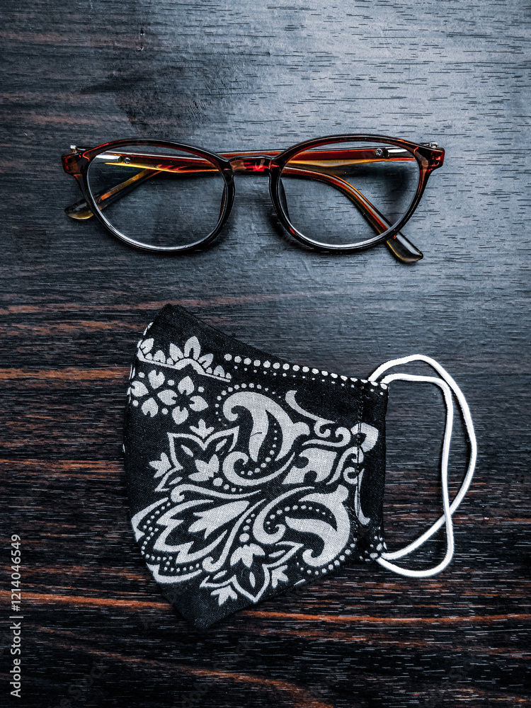 Stylish glasses and a handmade floral mask placed on a dark wooden table, creating an appealing contrast.