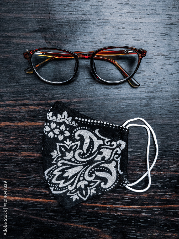 Stylish glasses and a handmade floral mask placed on a dark wooden table, creating an appealing contrast.