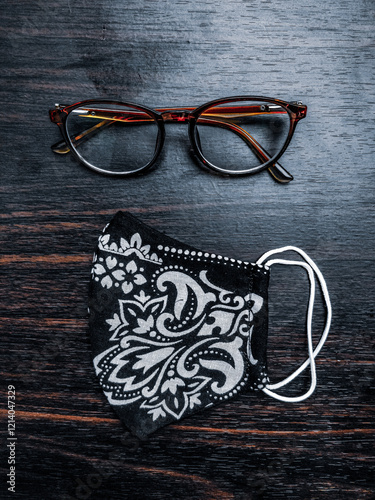 Stylish glasses and a handmade floral mask placed on a dark wooden table, creating an appealing contrast.