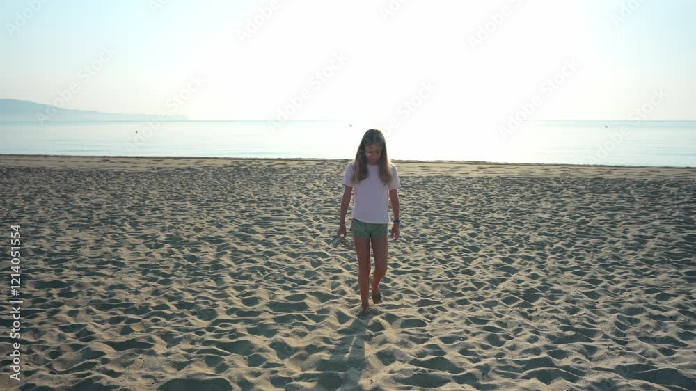 Young girl walking barefoot along golden sandy shoreline during sunrise, gently carrying sandals while enjoying peaceful morning seascape Young girl walking barefoot along golden sandy shoreline during sunrise, gently carrying sandals while enjoying peaceful morning seascape