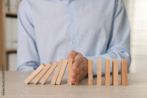Man stopping wooden blocks from falling at table, closeup. Domino effect