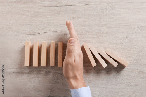 Man stopping wooden blocks from falling at table, top view. Domino effect