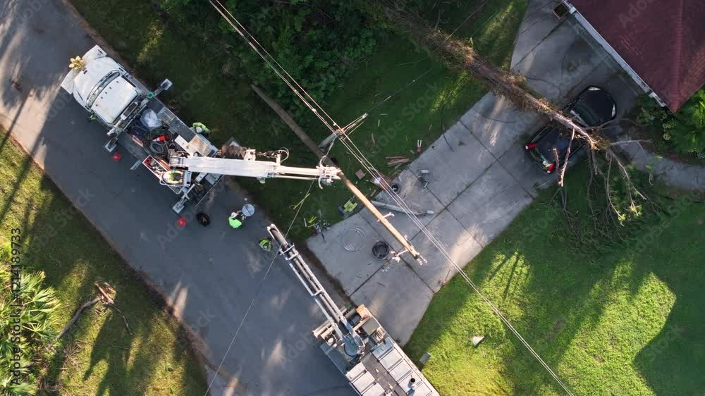 Hurricane aftermath in Florida. Workers using bucket trucks to repair blown down electrical wires at residential house. Utility services fixing damaged power lines.