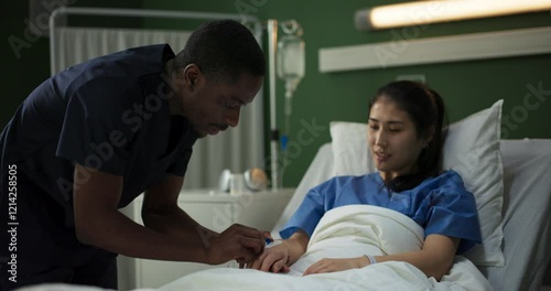 In a hospital room, a young African doctor puts a catheter on a woman injured in a car accident.