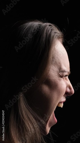 Profile portrait of an angry middle aged Caucasian woman screaming, standing over black background. Concept of an emotional stress. Vertical video.