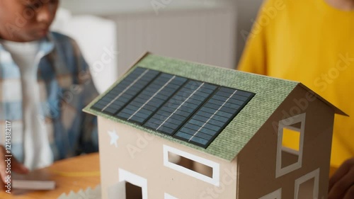 Close-up of solar-powered model house with roof and solar panels. This detailed shot highlights the progress made by African brothers as they collaborate on their school science project