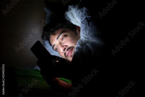 Young man lying in the bed and chatting on his smartphone at night	