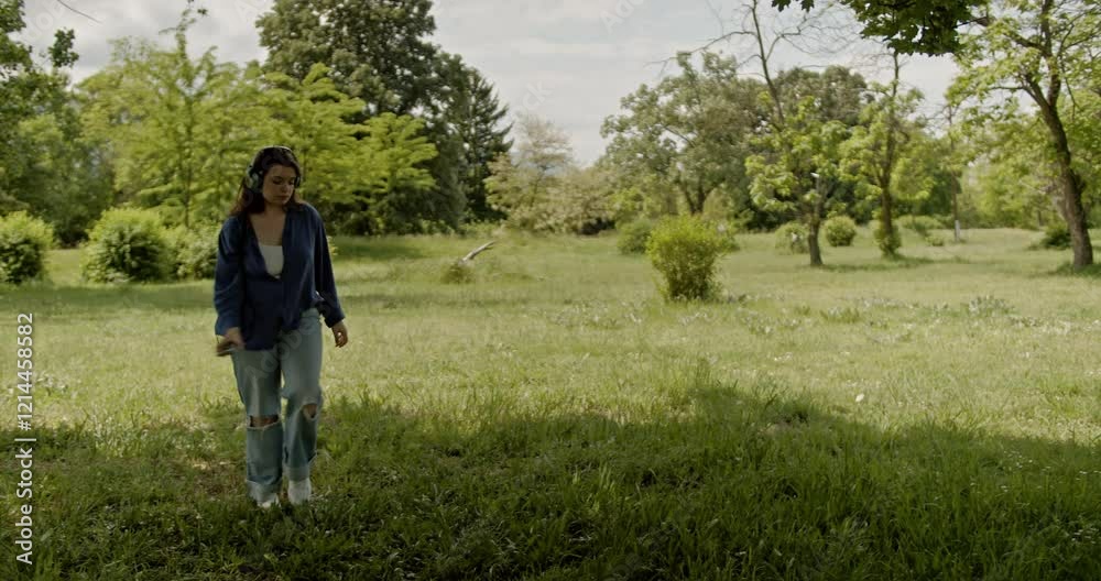 Carefree Young Woman Dances to Music on Headphones in a Sunny Green Meadow, Enjoying Freedom and Nature. Carefree Young Woman Dances to Music on Headphones in a Sunny Green Meadow, Enjoying Freedom and Nature.