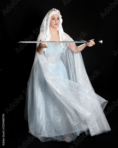 full length portrait beautiful blonde fantasy maiden faery wearing medieval fairytale ballgown costume, flowing white hooded cape. standing pose holding a sword weapon, isolated dark studio background photo