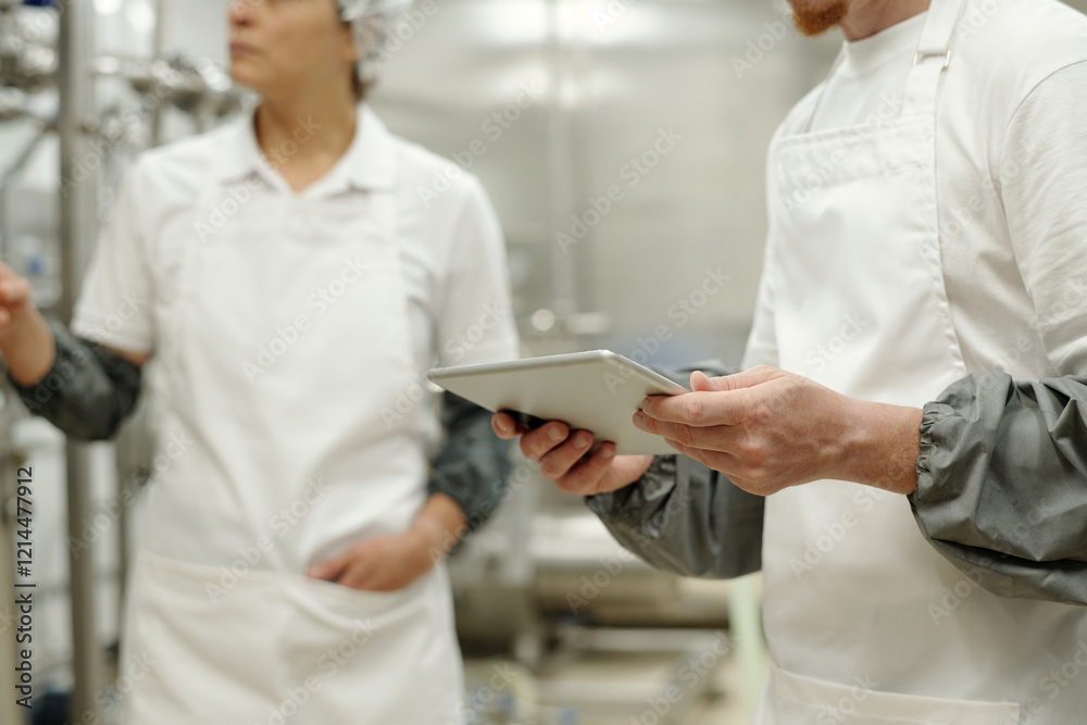 Workers inspecting food processing equipment in modern factory setting, wearing hygienic protective clothing, holding tablet device for monitoring and recording data Workers inspecting food processing equipment in modern factory setting, wearing hygienic protective clothing, holding tablet device for monitoring and recording data