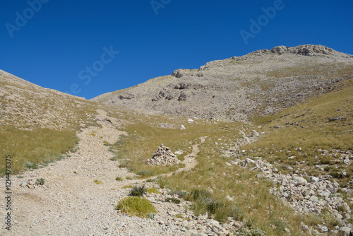 Hiking trail on the southern part of the island of Krk in Croatia defined by a barren, rocky terrain dotted with patches of resilient vegetation, peak Bag on the right photo