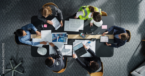 Top Down View of Diverse Team of Real Estate Construction Engineers Discussing Blueprints, Documents in Corporate Office. Modern Workspace of Architectural Bureau with Colleagues Using Tablet, Laptop