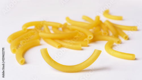 Dry tube shaped curved macaroni on white background. Close up photograph with selective focus on one single pasta.