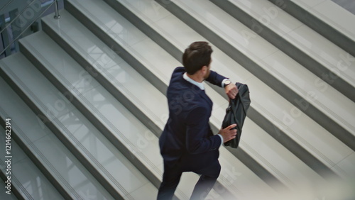 Hurrying businessman carrying briefcase climbing stairs inside office interior.