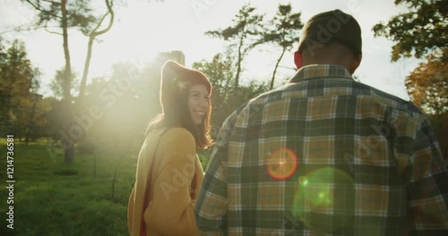 Rear view of a happy brunette girl in a yellow sweater walking and drinking coffee with her boyfriend during a date in a sunny autumn park