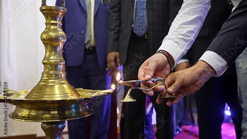 Close-up of a man's hands lighting a large oil lamp with a smaller oil lamp during an event