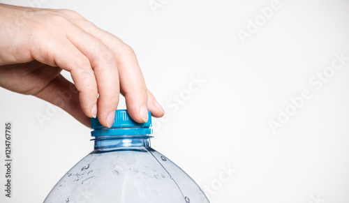 plastic cap of water bottle is opened by female hands on light background close-up
