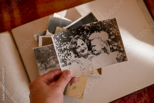 Female hand is holding black and white old photo of her grandmother with her daughter. Vintage photo album with photos. Family and life values concept. Mother and her little girl