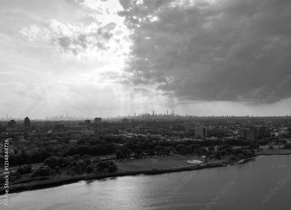 Fototapeta premium aerial view of new york city skyline from corona flushing meadows park with dramatic dark sky coming clouds at sunset (lake distant skyscrapers of manhattan far away) horizon silhouette shadow queens