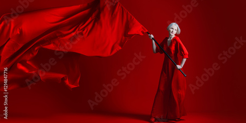 Rebel, a concept. The revolution. A woman in a red dress waves a huge red flag on a red background.