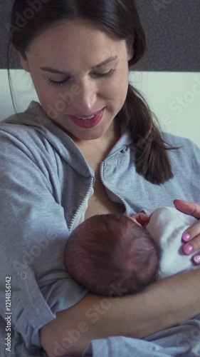 Joyful Caucasian middle aged mother breastfeeding newborn baby at home. Motherhood, lactation and nourishment concept. Vertical video.