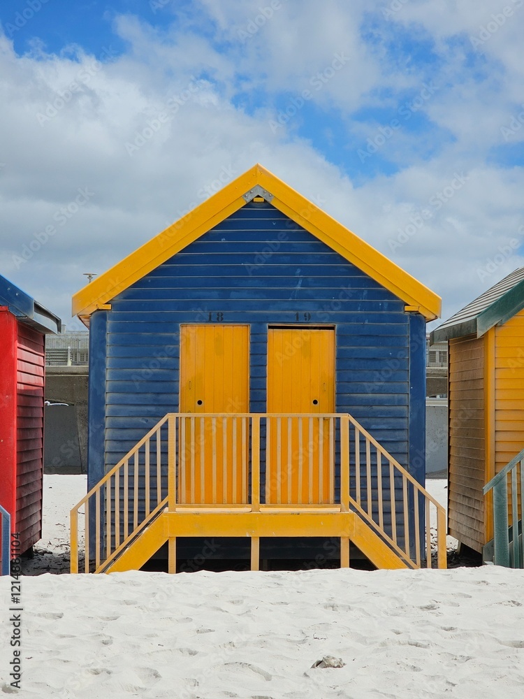 Naklejka premium Colorful wooden beach huts lining sandy muizenberg coastline, framing azure sky and pristine white landscape near cape town, south africa