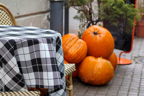 
A corner of the cafe's outdoor terrace, where several orange pumpkins are placed next to each other on a table with a checkered tablecloth. photo